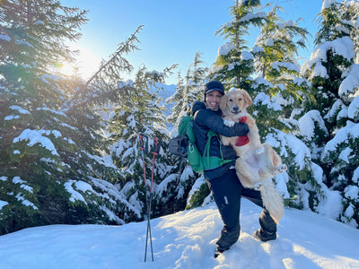 A woman picks up her golden retriever dog and poses with him in the snow. 