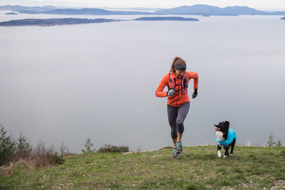 Krissy & PD in Wind Sprinter Jacket run up grassy slope above clouds in the hills.