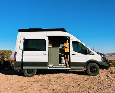 A woman and her dog stand in a camper van. 